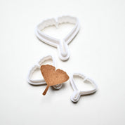Three white plastic ginkgo leaf cookie cutters in various sizes with a baked ginkgo-shaped pastry.