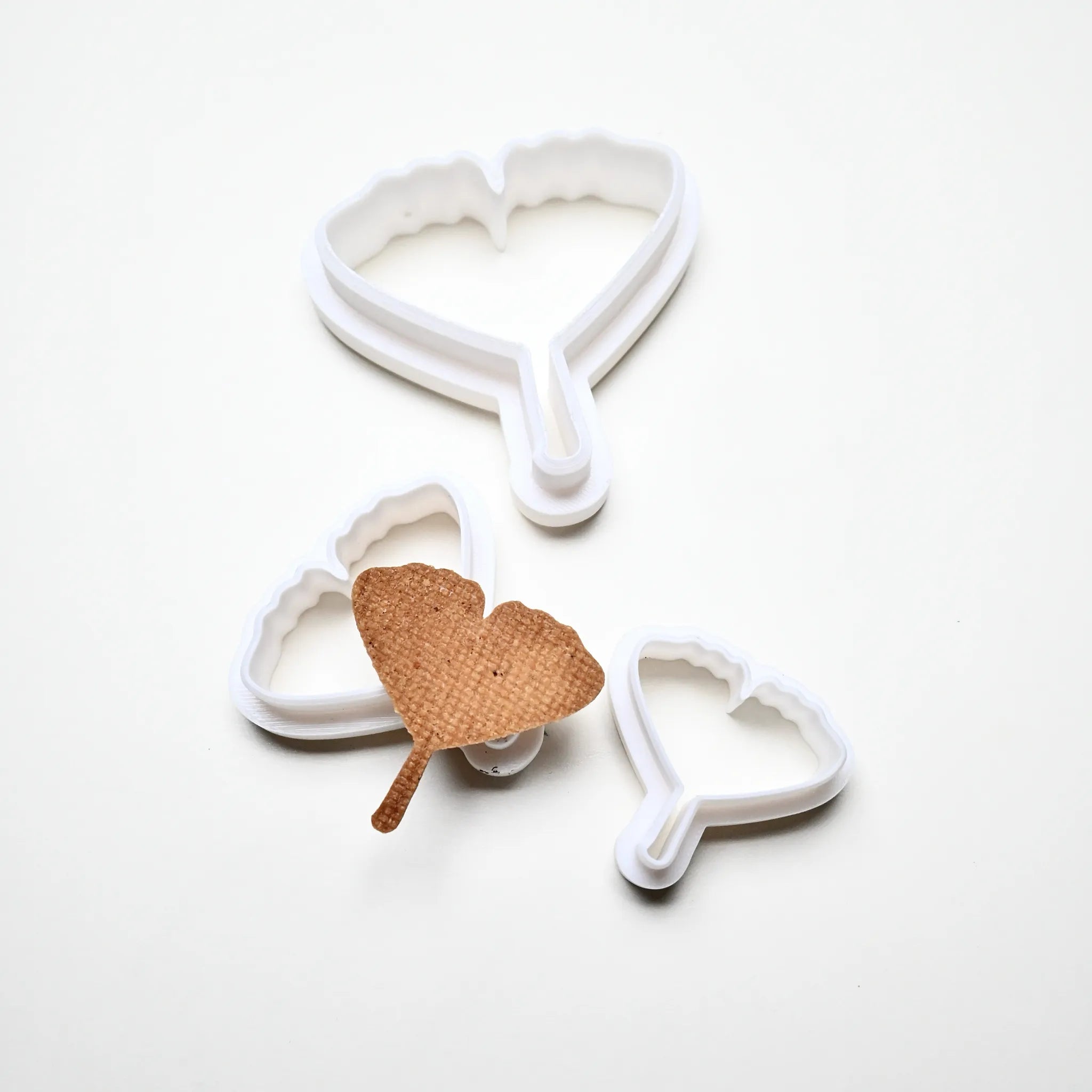 Three white plastic ginkgo leaf cookie cutters in various sizes with a baked ginkgo-shaped pastry.