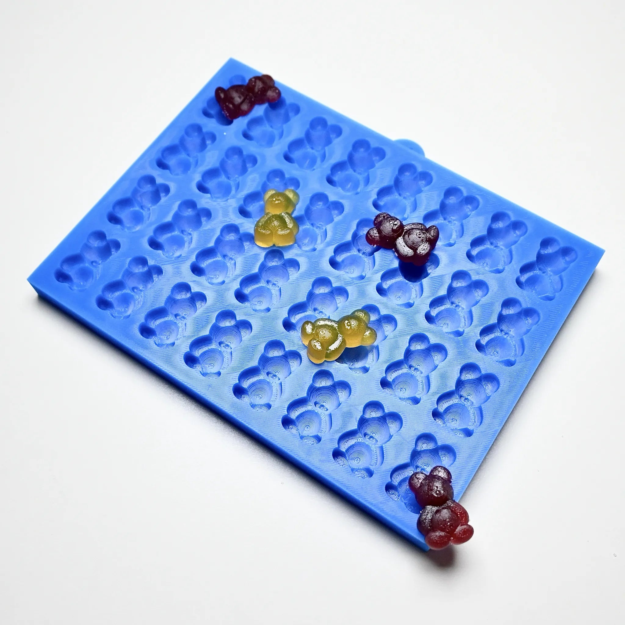 Blue silicone mold with miniature bear-shaped cavities and colorful gummy bears.