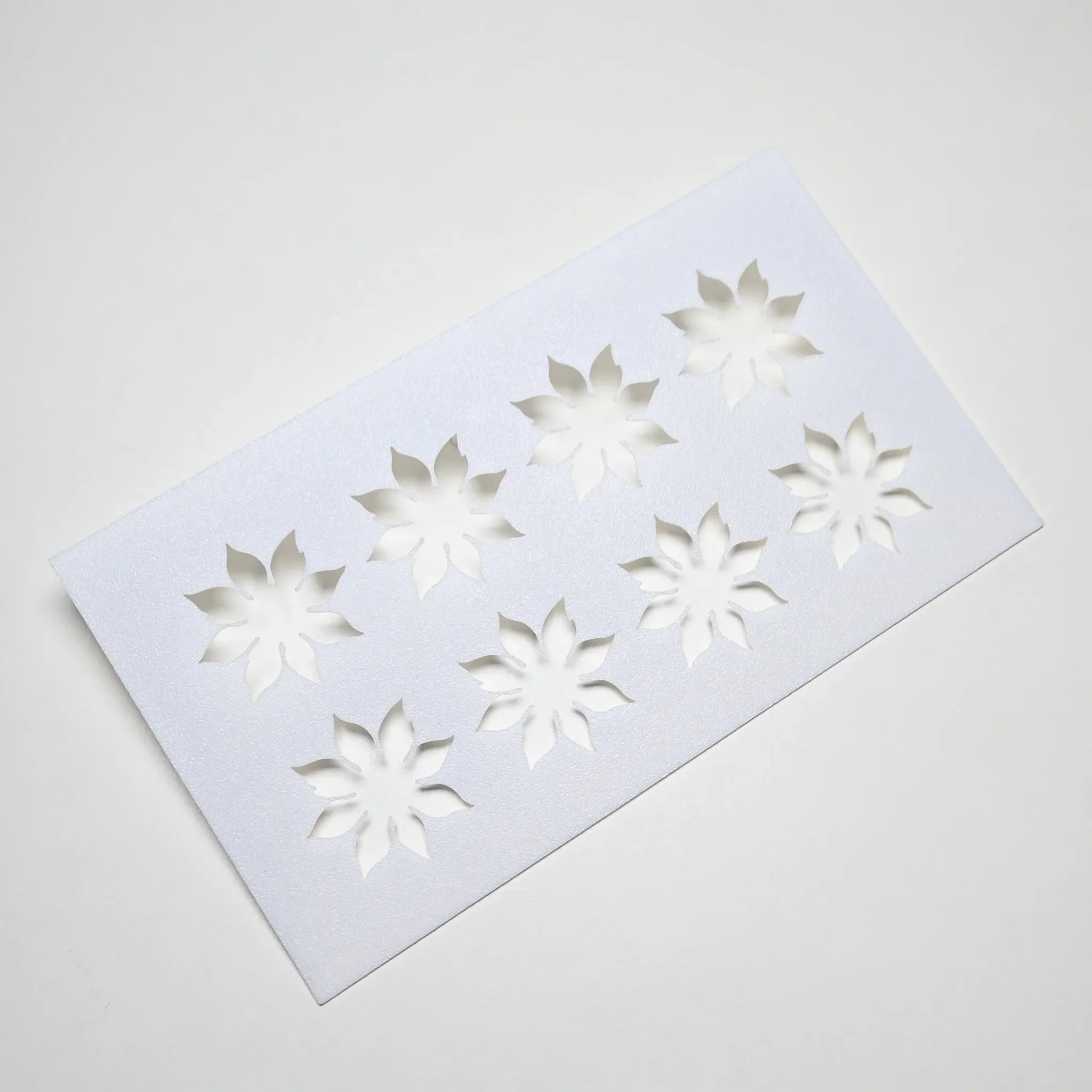 White plastic pastry stencil with eight strawberry calyx star-shaped cutouts.