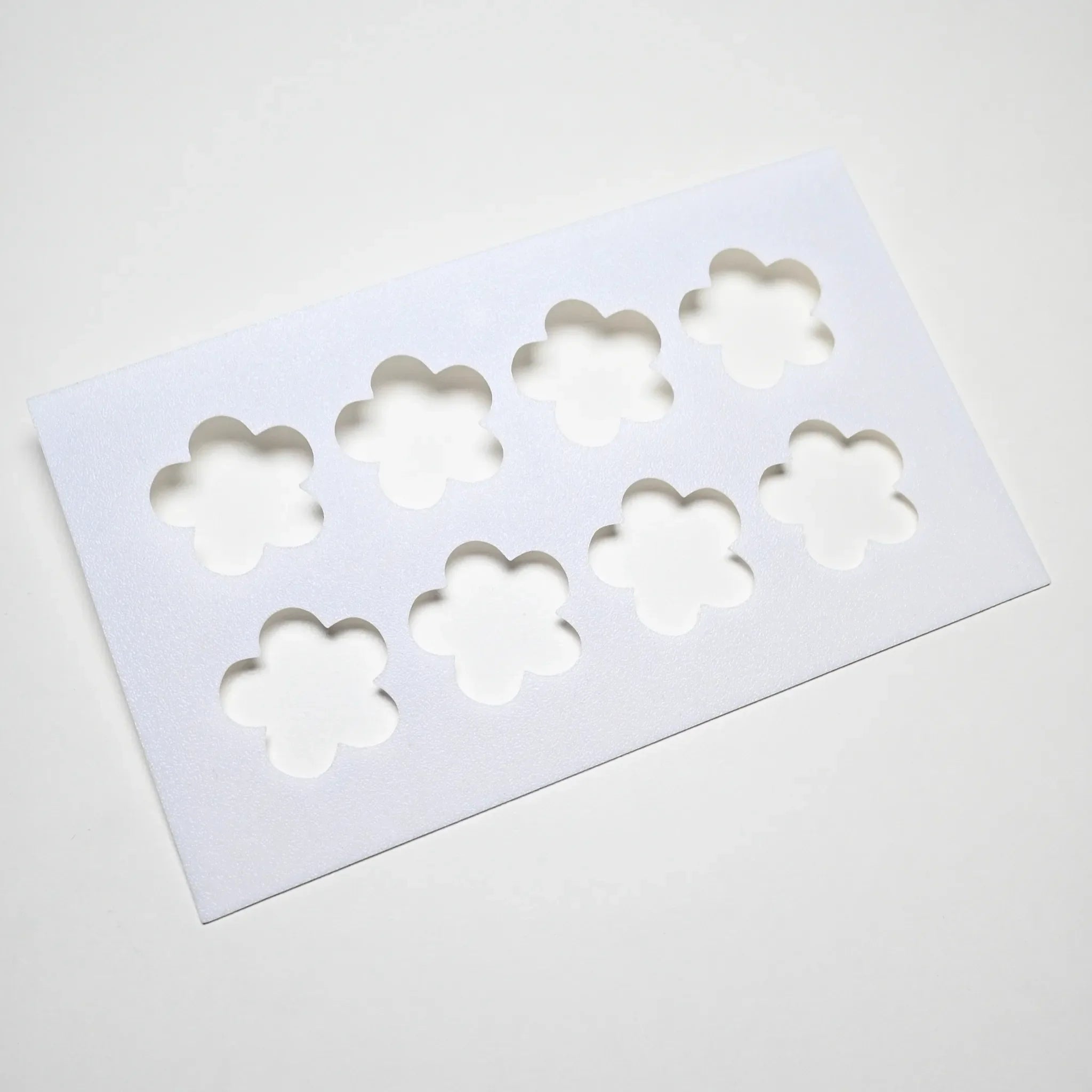White plastic pastry stencil with eight strawberry flower shaped cutouts.