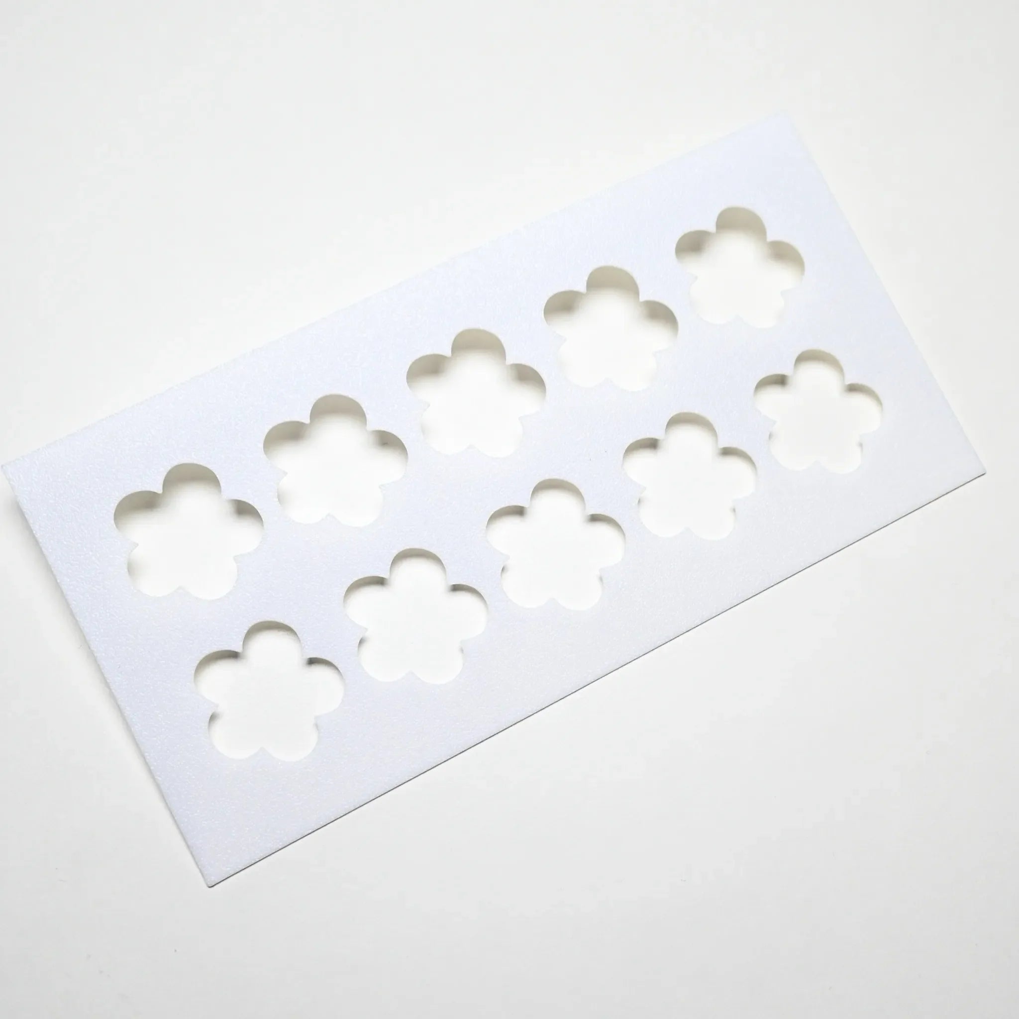 White plastic pastry stencil with ten five-petal strawberry flower cutouts.