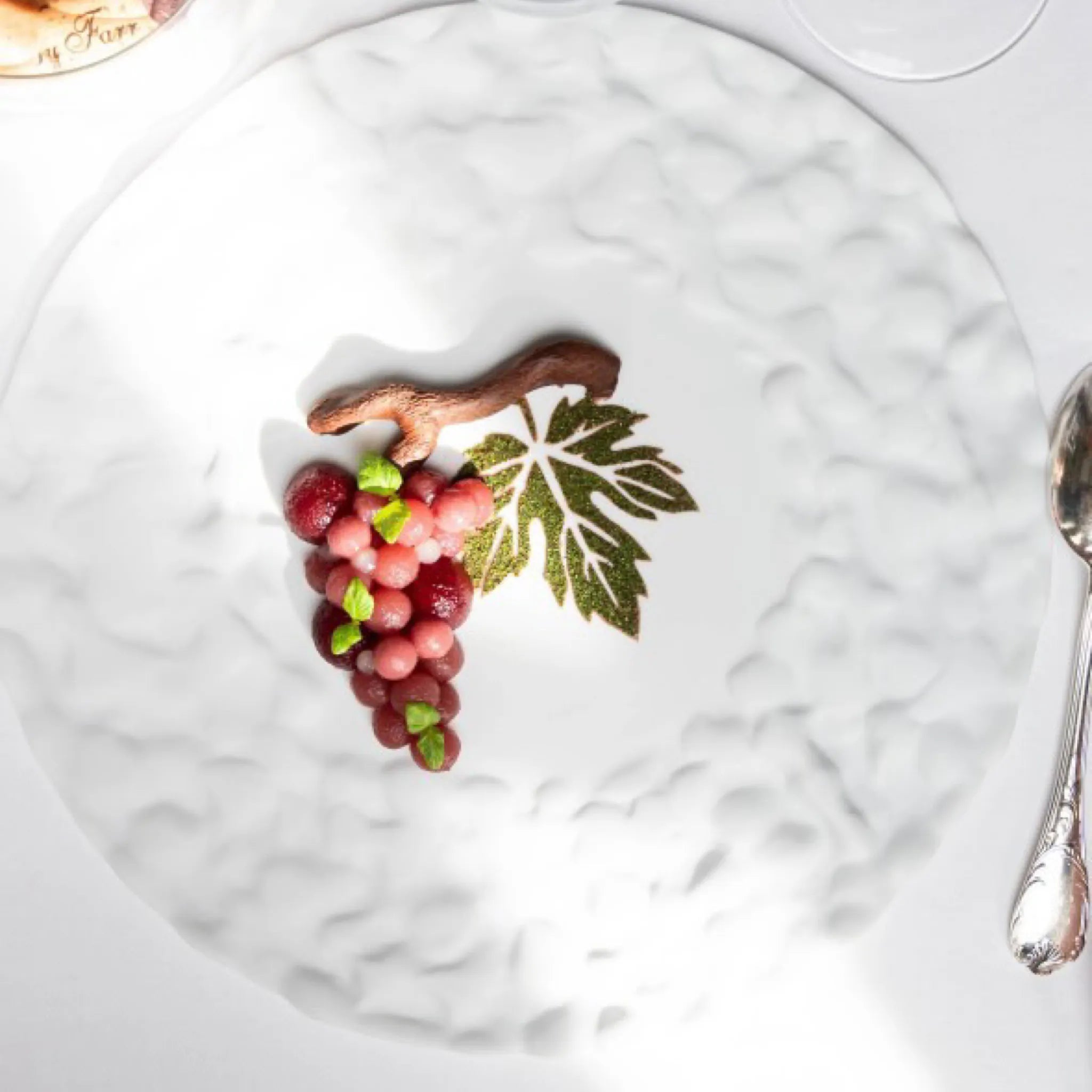 Green vine leaf stencil design on a white plate with a grape-shaped dessert.