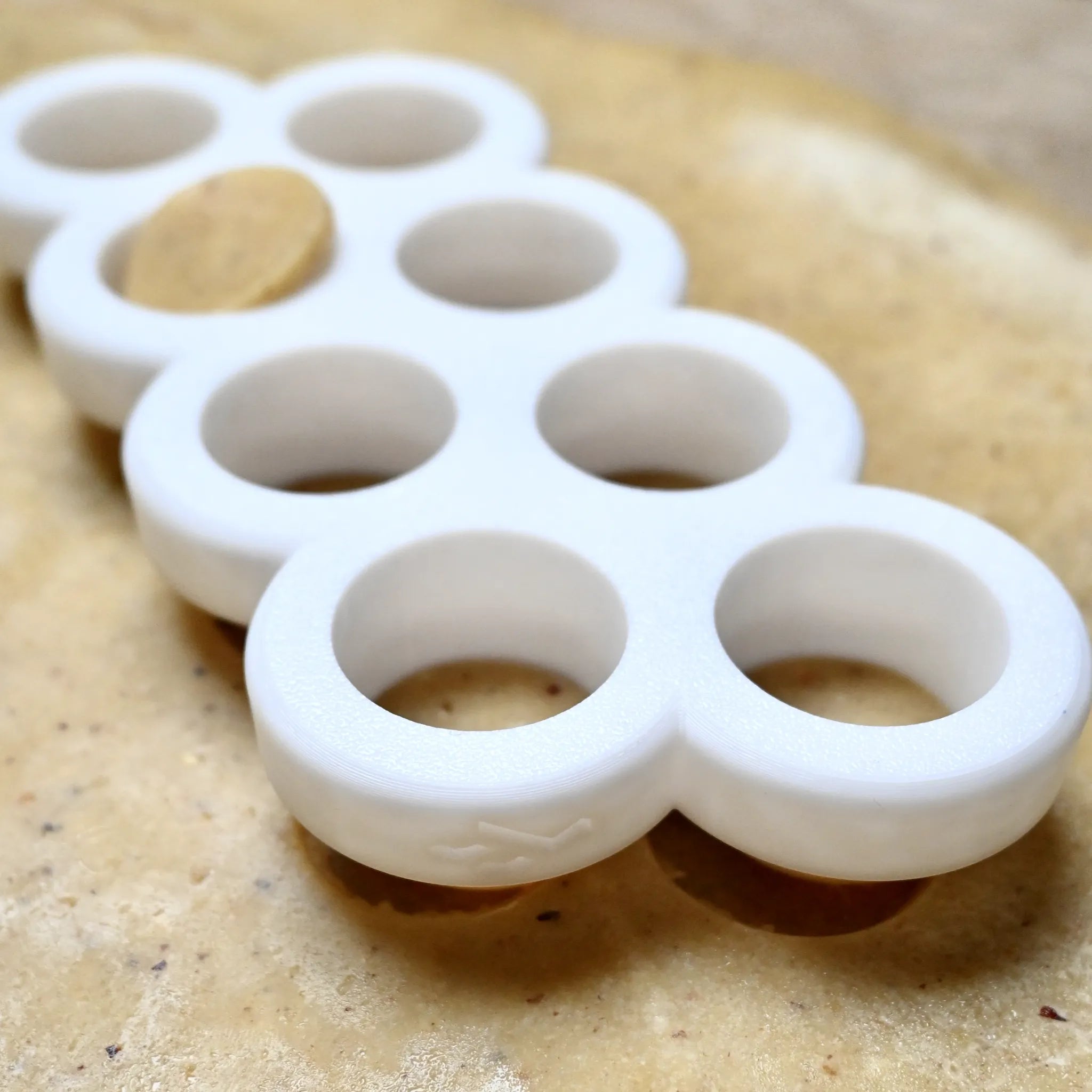 White plastic multi circle cookie cutter on rolled-out dough, cutting round shapes.