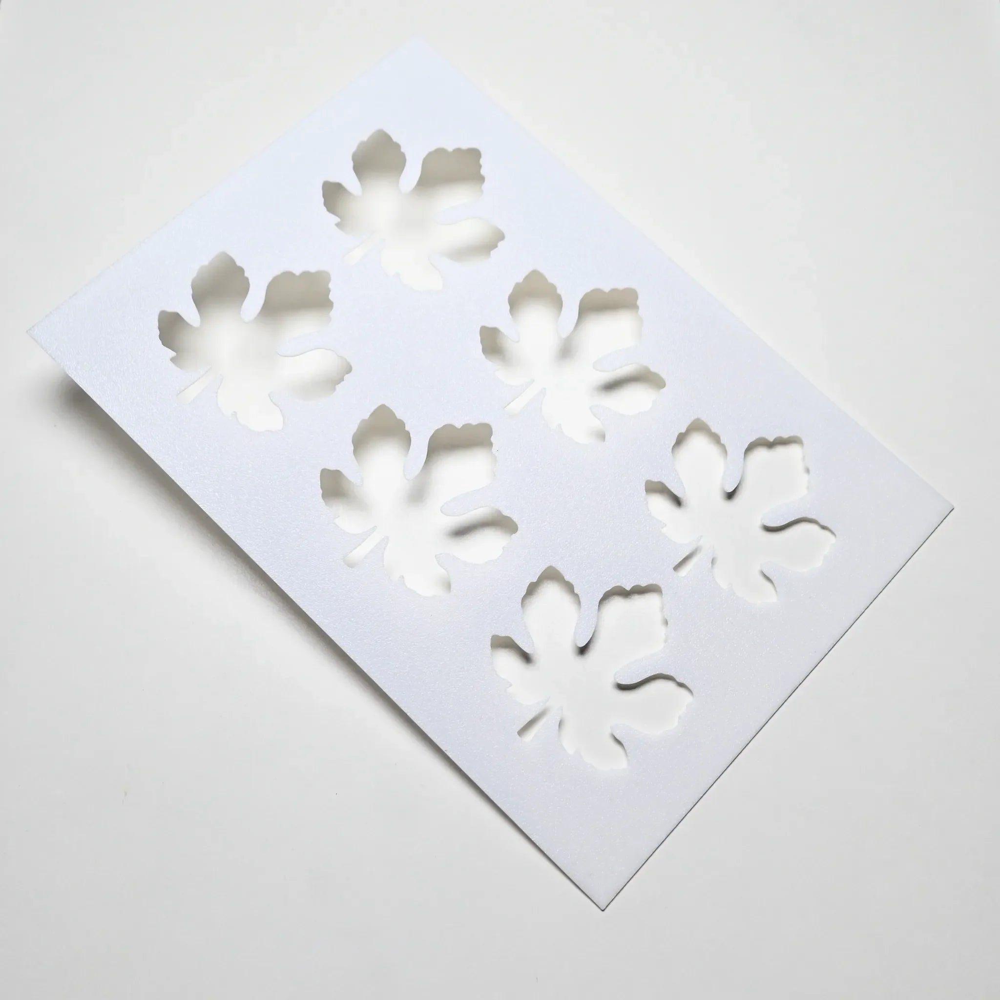 White plastic pastry stencil featuring six detailed fig leaf cutouts.