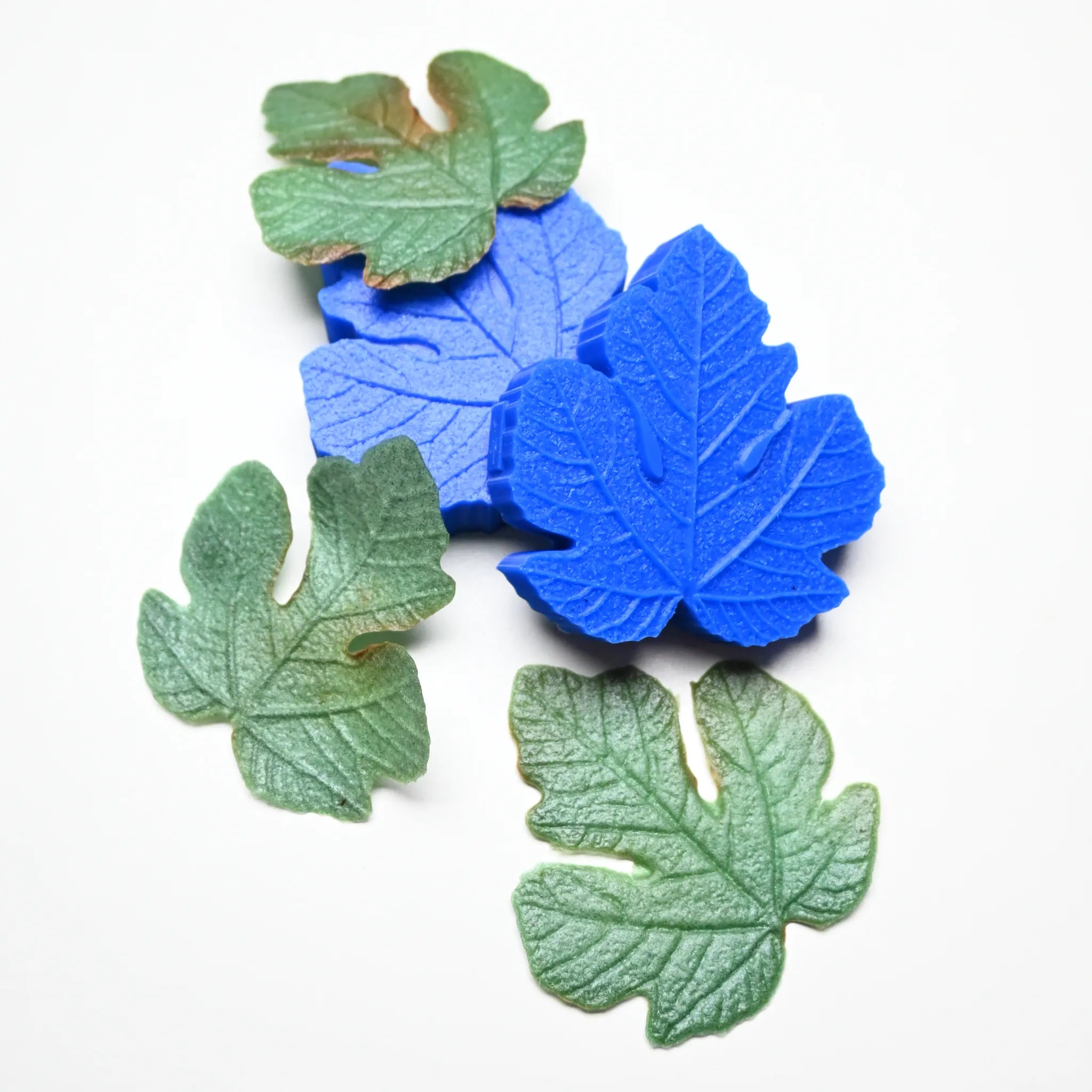 Blue silicone fig leaf veiner molds with realistic green edible paste leaves.