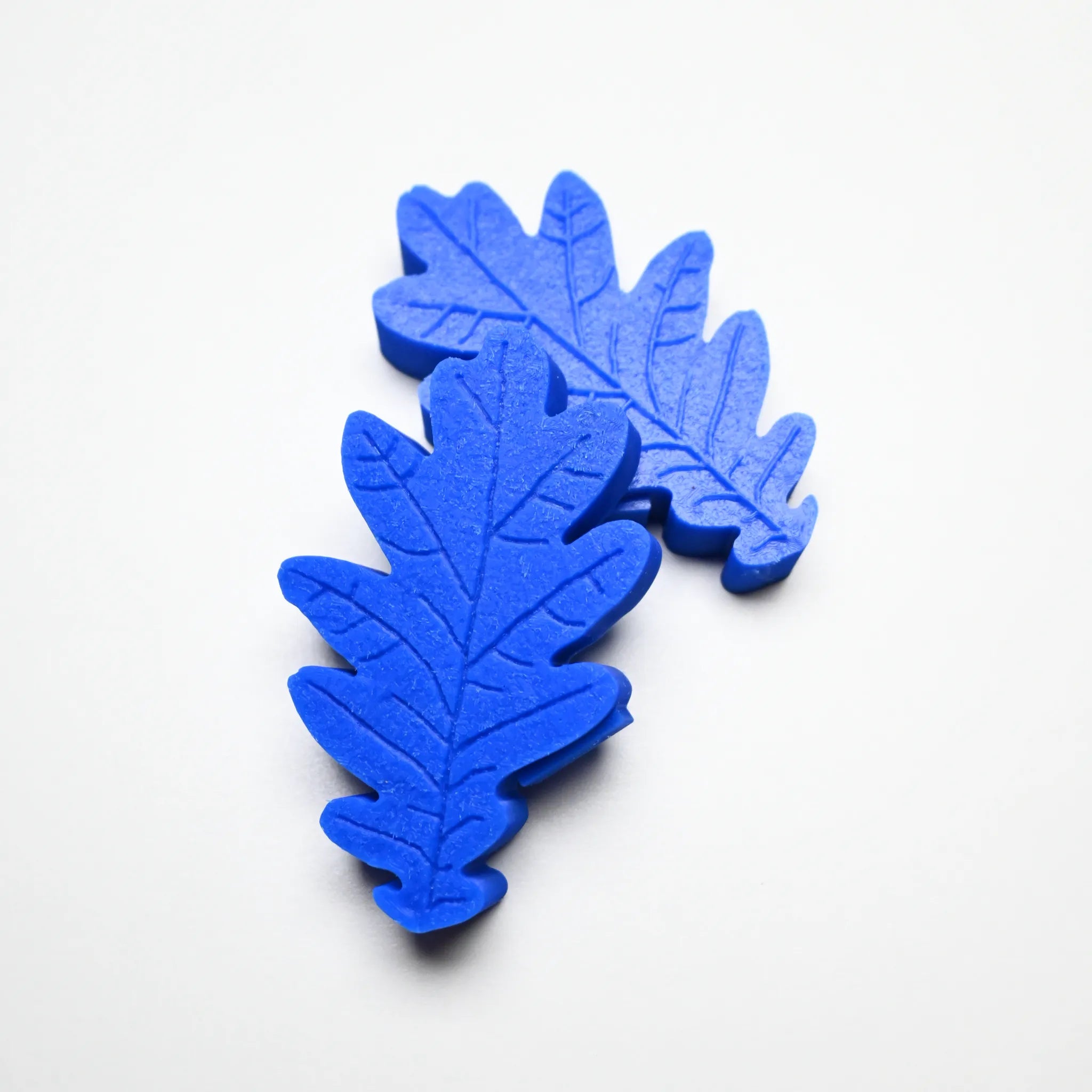 Two blue silicone oak leaf pastry molds with detailed vein textures on a white background.