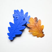 Two blue silicone oak leaf molds with detailed veins next to a realistic brown pastry leaf.