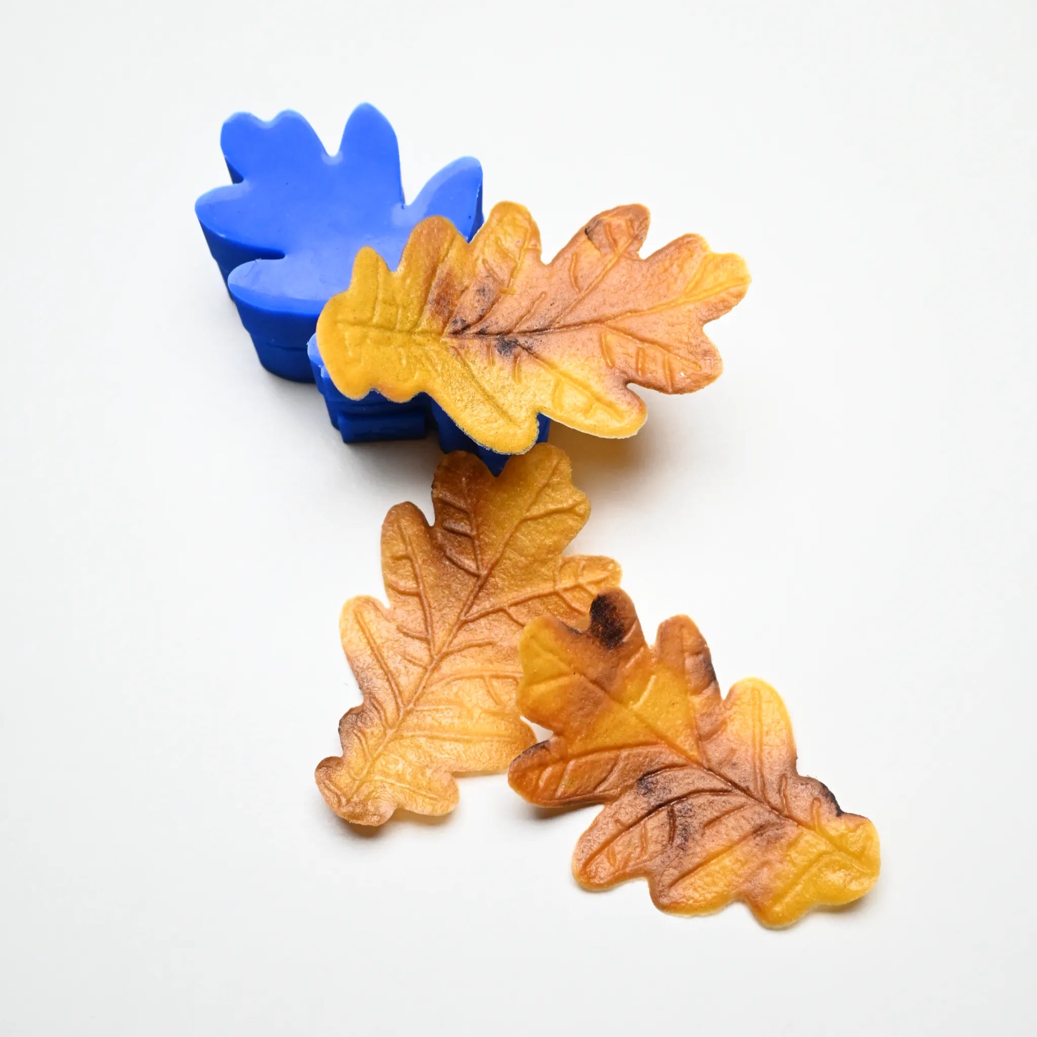 Blue silicone oak leaf mold with realistic yellow and brown pastry leaves showing detailed vein textures.