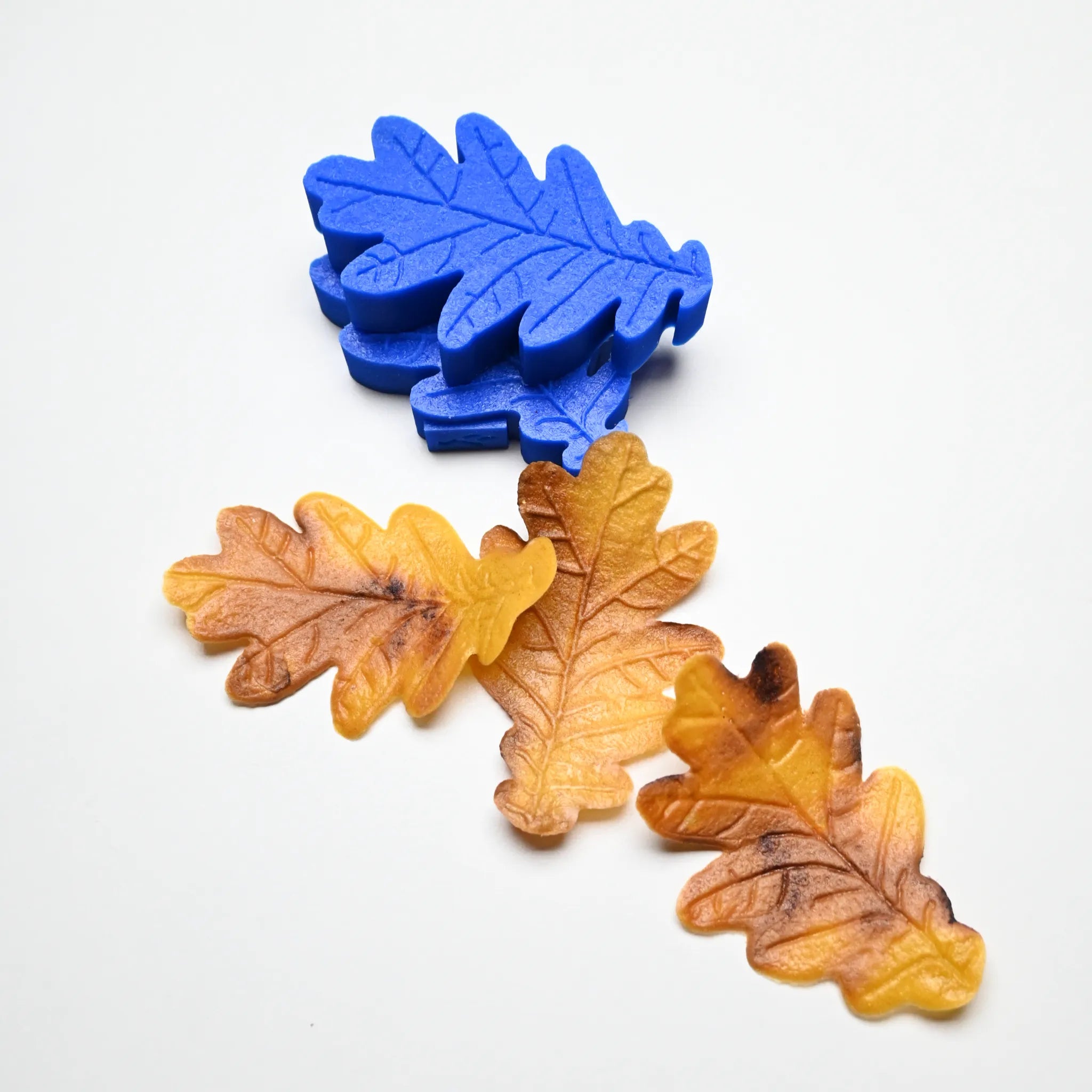 Blue silicone oak leaf mold with detailed veins, shown alongside realistic brown and yellow pastry leaves.