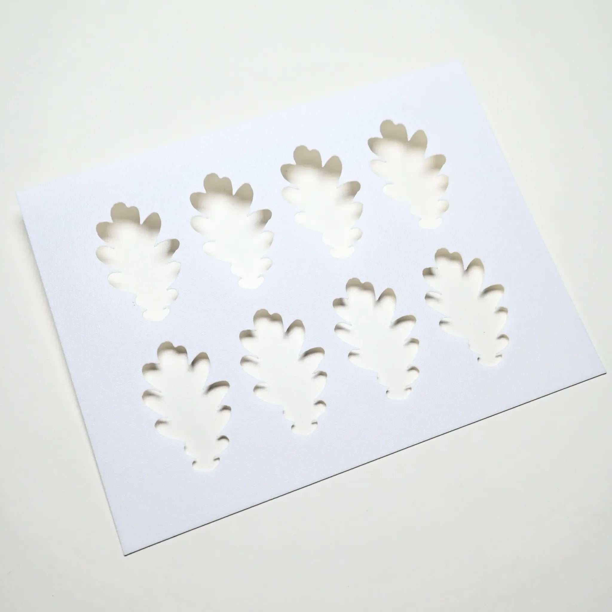 White plastic pastry stencil featuring eight detailed oak leaf cutouts.