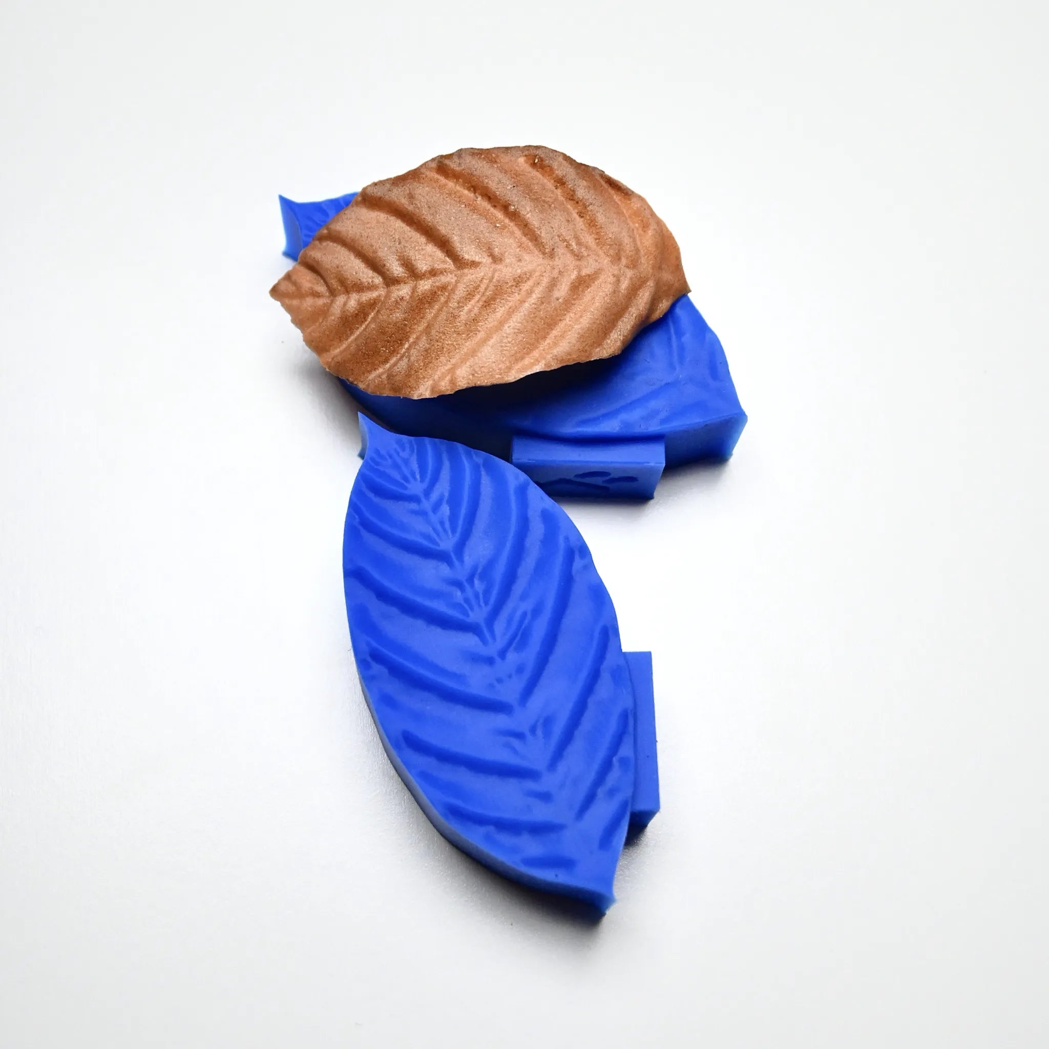 Blue silicone coffee leaf molds with a textured brown pastry leaf on top.