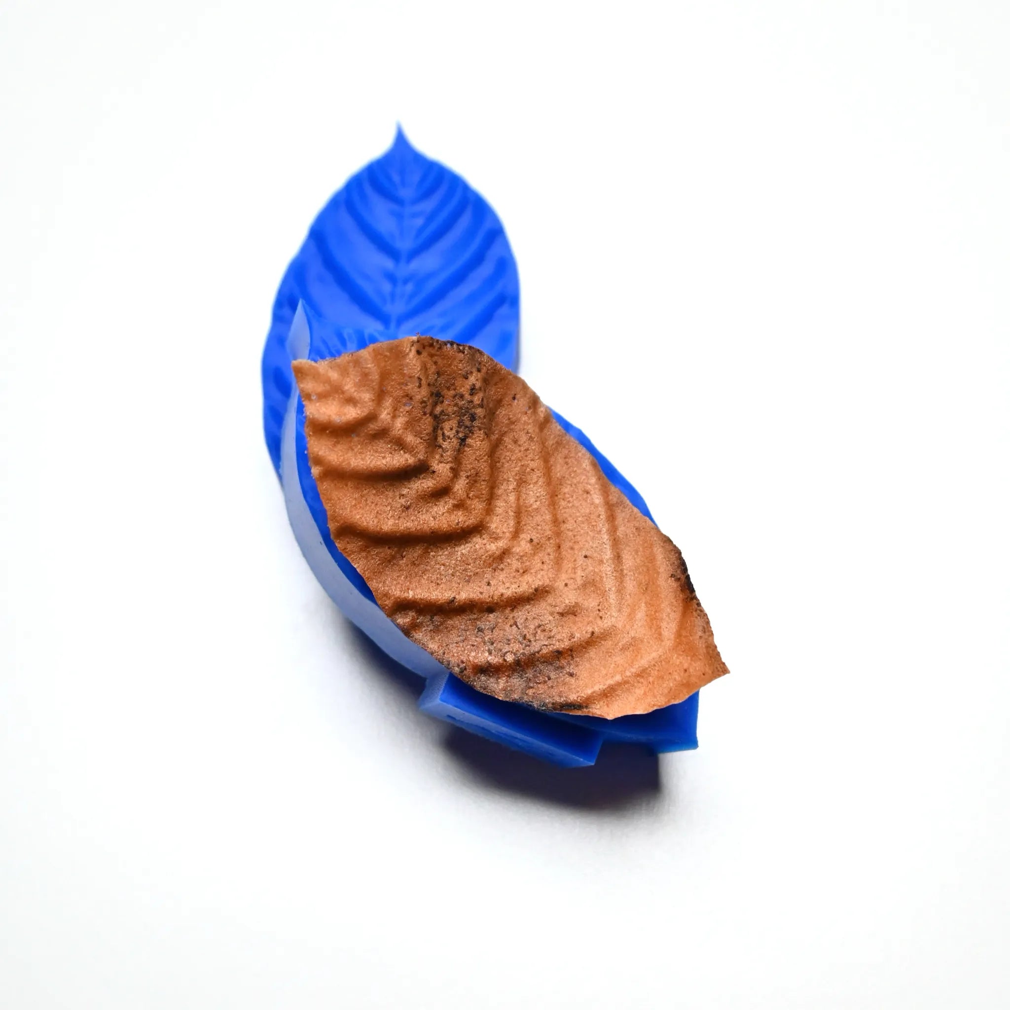 Blue silicone coffee leaf press mold with a textured brown edible leaf garnish.