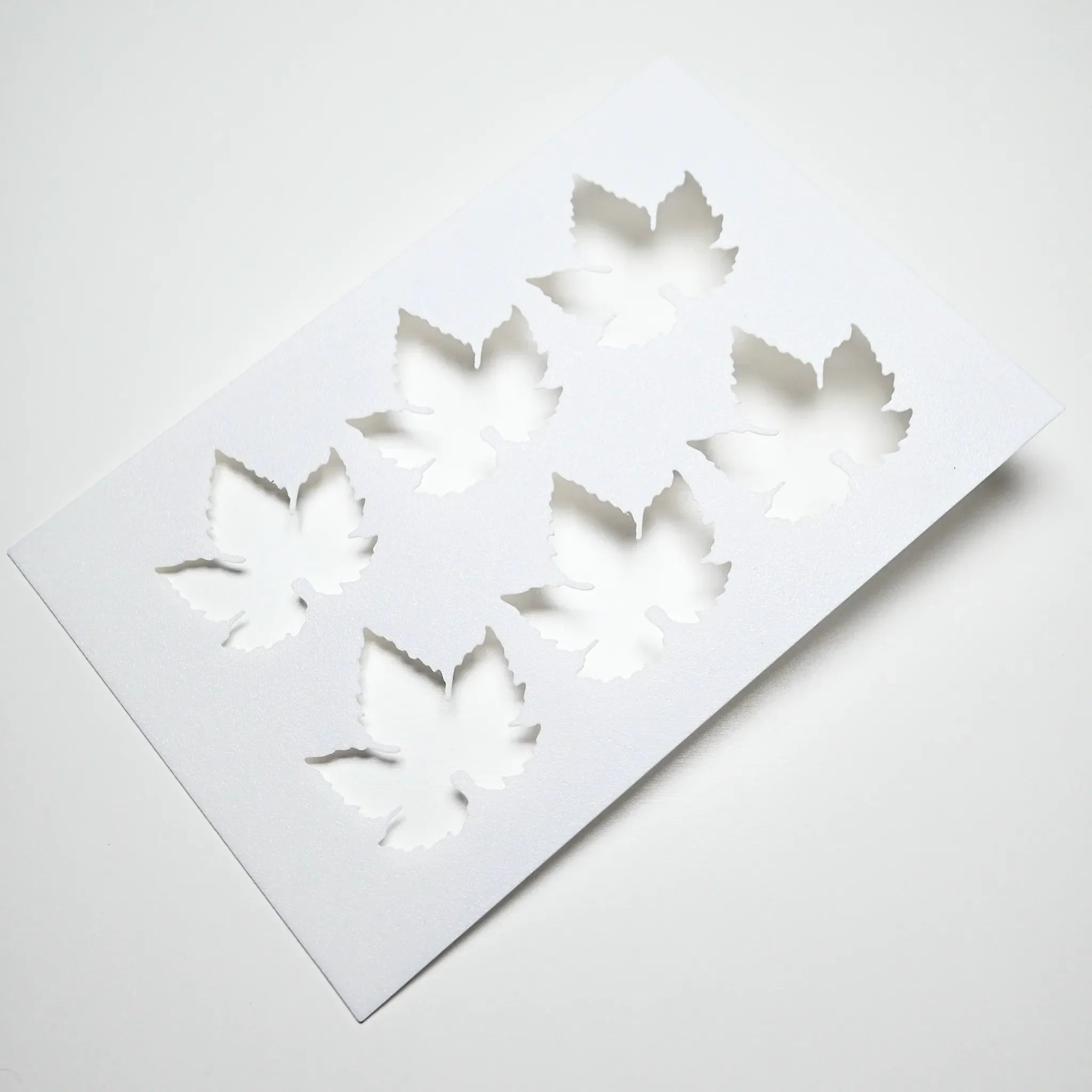 White flexible culinary stencil featuring six detailed vine leaf cutouts.