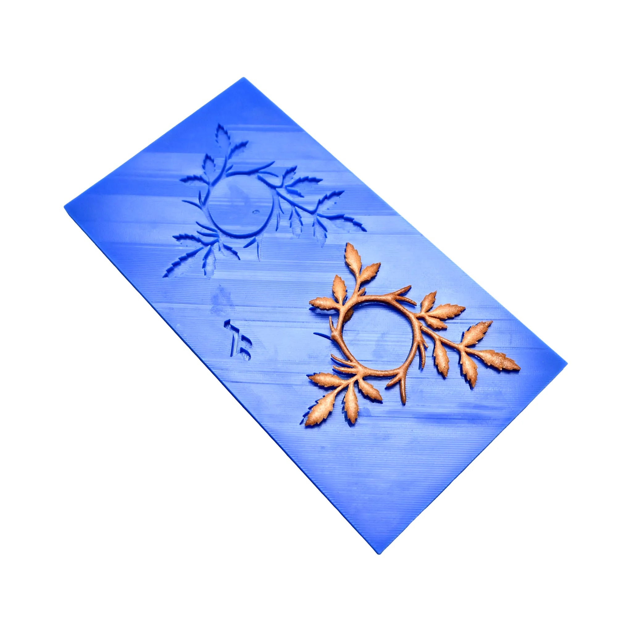 Blue silicone Tagelia tuile mat with a leaf-wreath mold and a finished golden pastry.