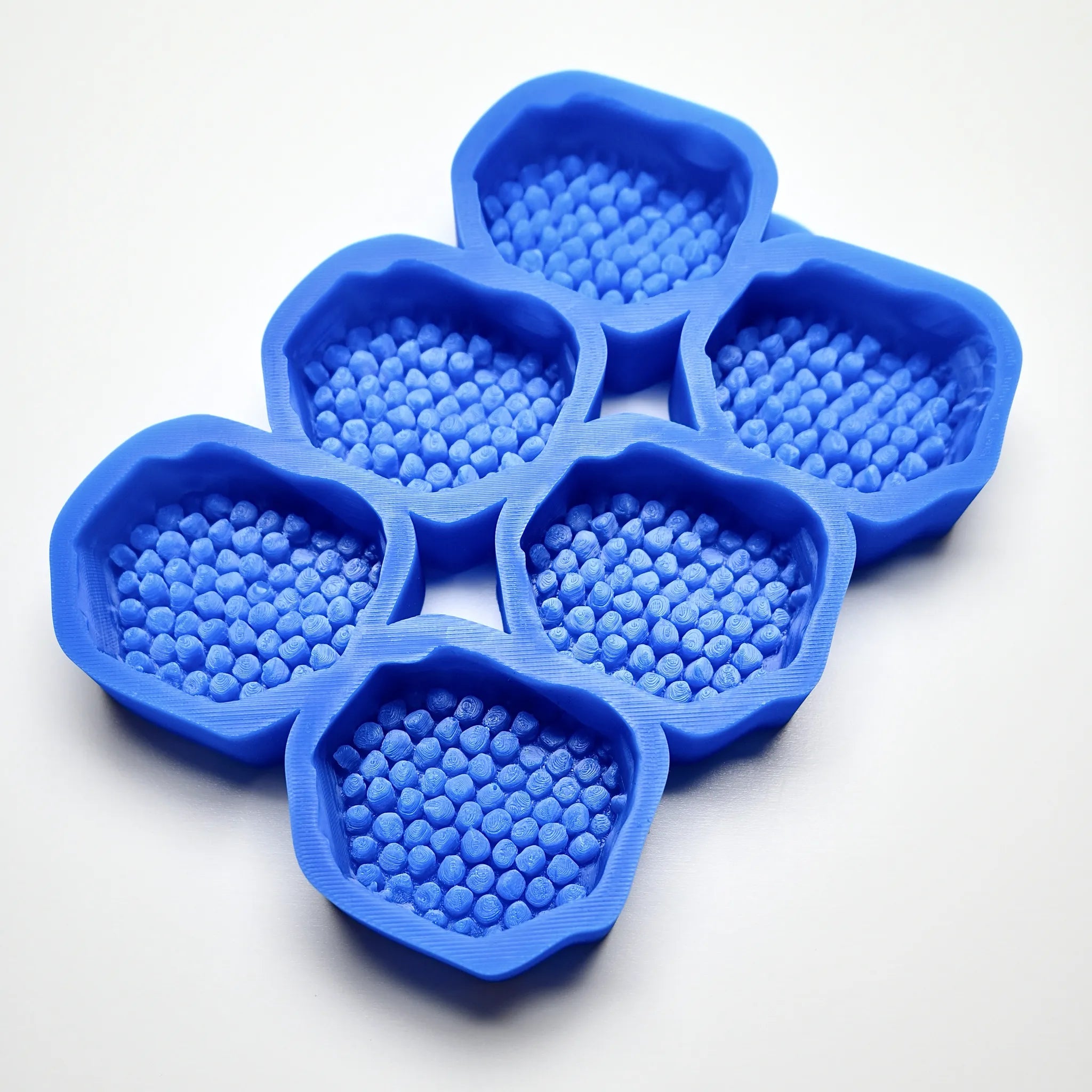 Blue silicone mold with six hexagonal cavities featuring textured honeycomb patterns.
