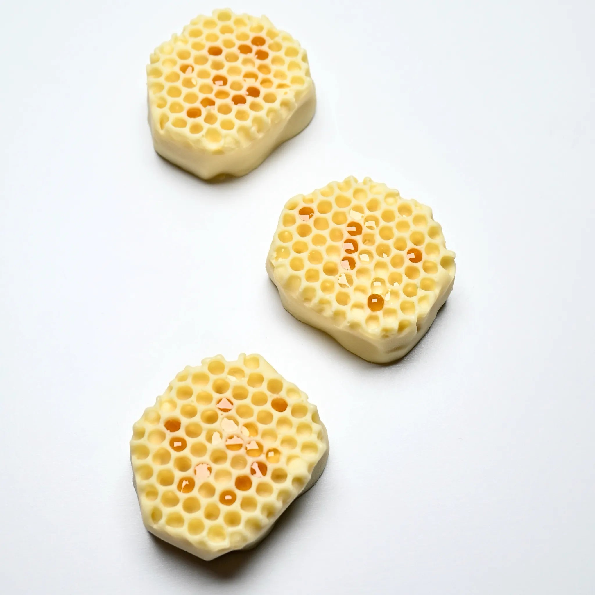 Three hexagonal white chocolate honeycomb treats with realistic cell textures and honey drops.