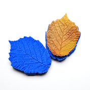 Blue silicone hazelnut leaf press molds with detailed vein textures and a golden pastry leaf.