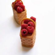 Two woven basket-shaped pastries filled with fresh red raspberries on a white background.