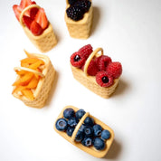 Five woven basket-shaped pastries filled with fresh berries and sliced fruit on a white background.