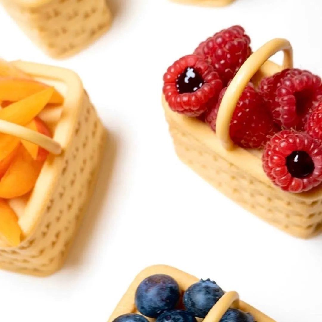 Woven basket-shaped pastry molds filled with fresh raspberries, blueberries, and sliced peaches.